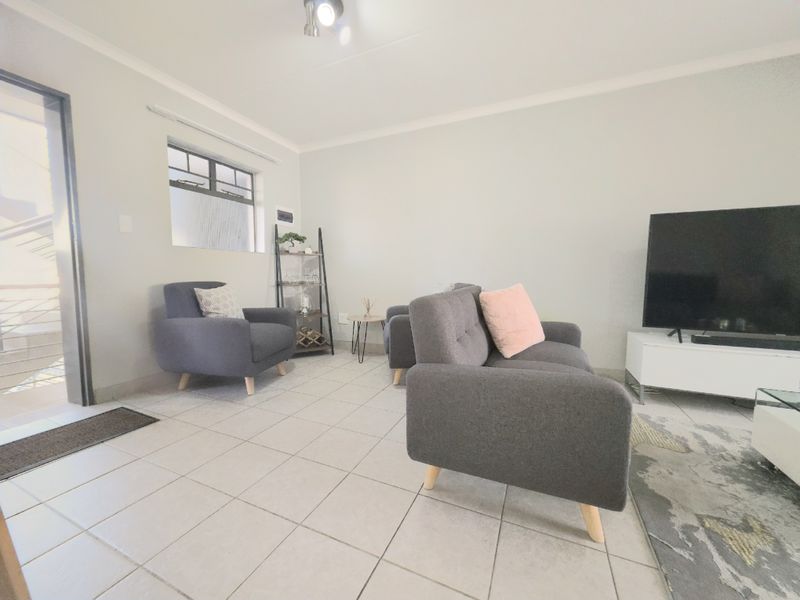 A bright living room featuring neutral tiled flooring, a sliding glass door providing outdoor access, and clean wall finishes.