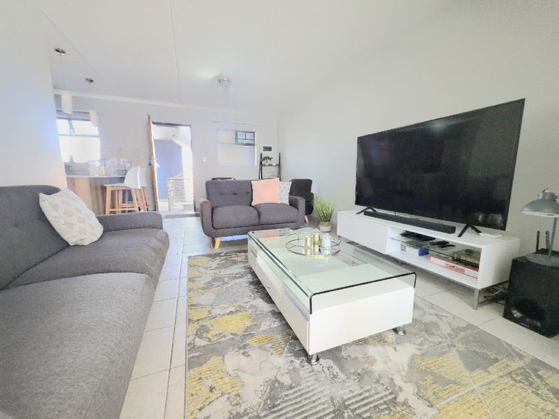 Open-plan living area featuring tiled flooring and a connected kitchen space with a breakfast bar, providing a functional and versatile layout.