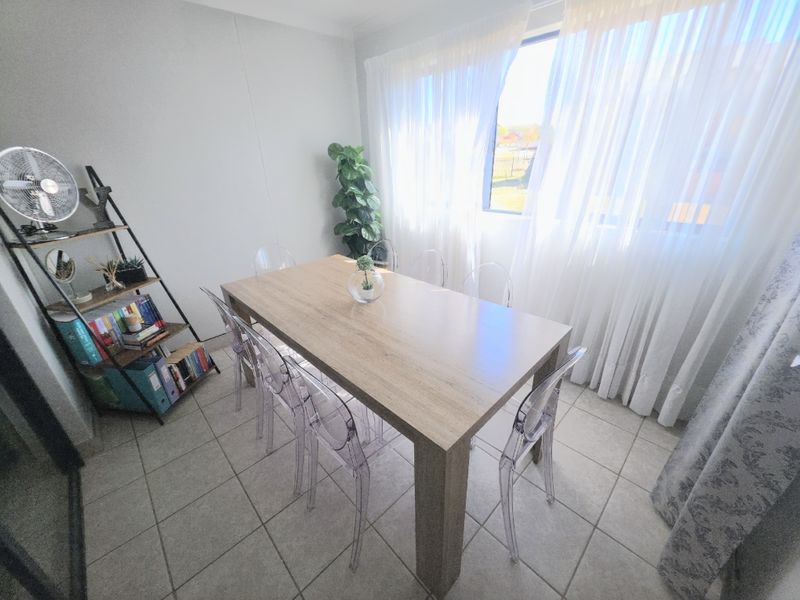 A bright dining room featuring neutral tiled flooring and a large window with sheer curtains, providing ample natural light.