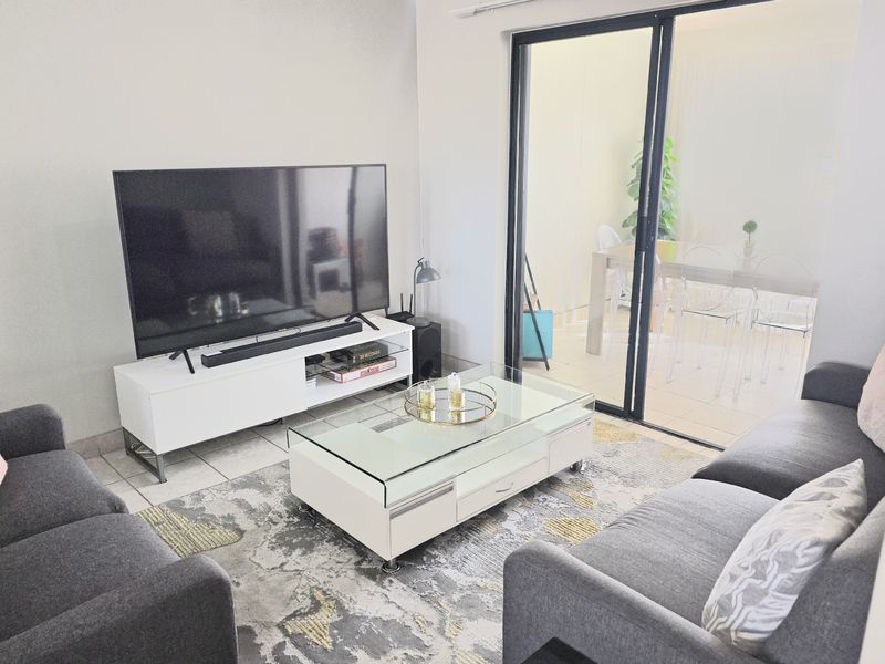 A bright living room featuring tiled flooring and a large sliding glass door that provides access to an adjacent patio area.