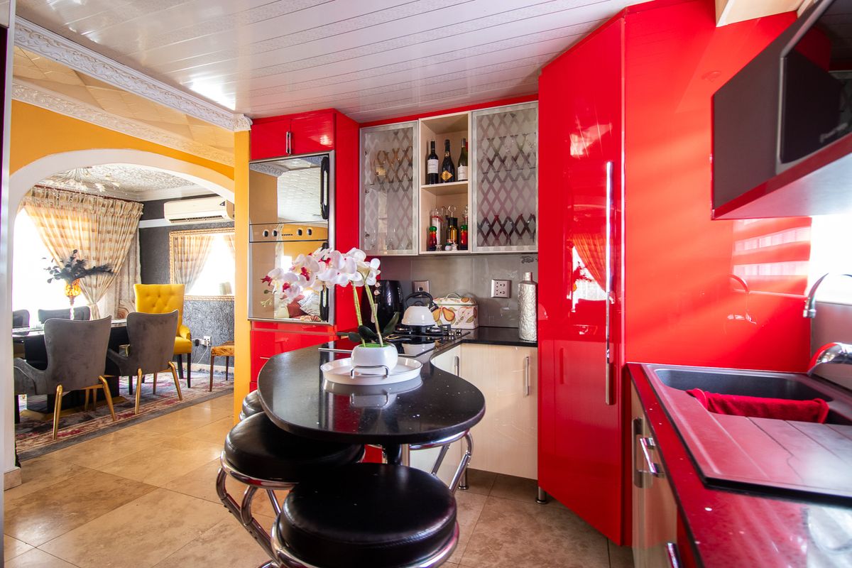 Vibrant kitchen featuring high-gloss red cabinetry, black granite countertops, and a built-in breakfast bar, seamlessly flowing into the adjacent dining area.