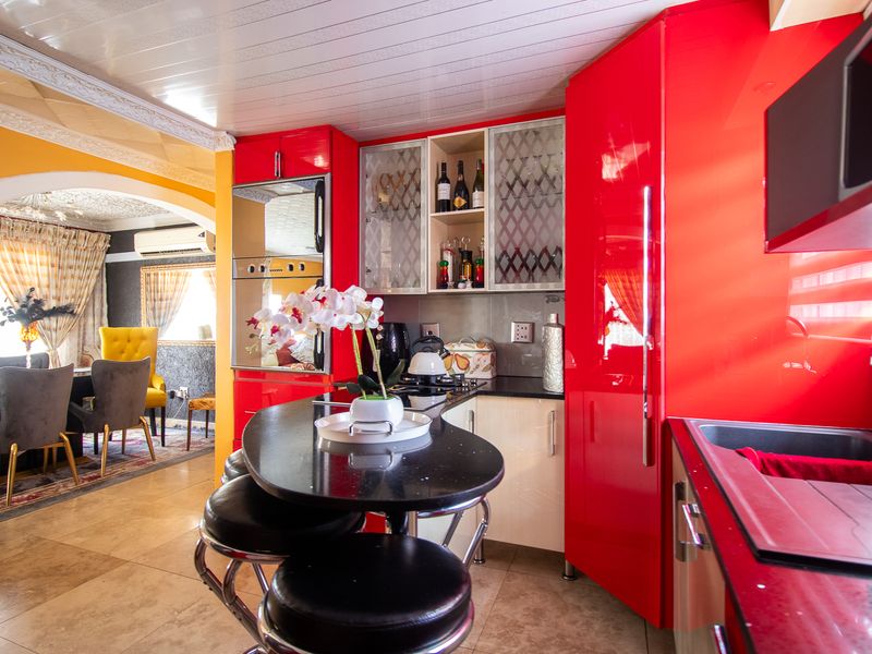 Vibrant kitchen featuring high-gloss red cabinetry, black granite countertops, and a built-in breakfast bar, seamlessly flowing into the adjacent dining area.
