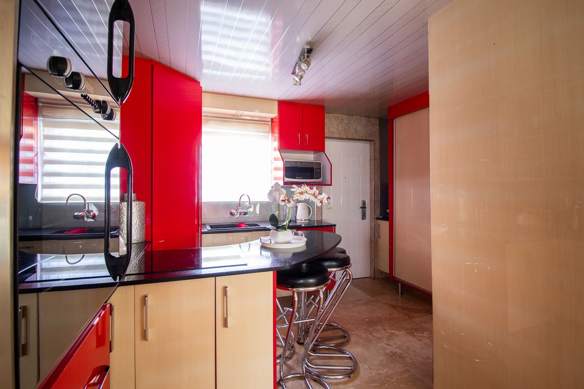 A compact kitchen featuring vibrant red and light wood cabinetry, black granite countertops, and tiled flooring with integrated appliances.