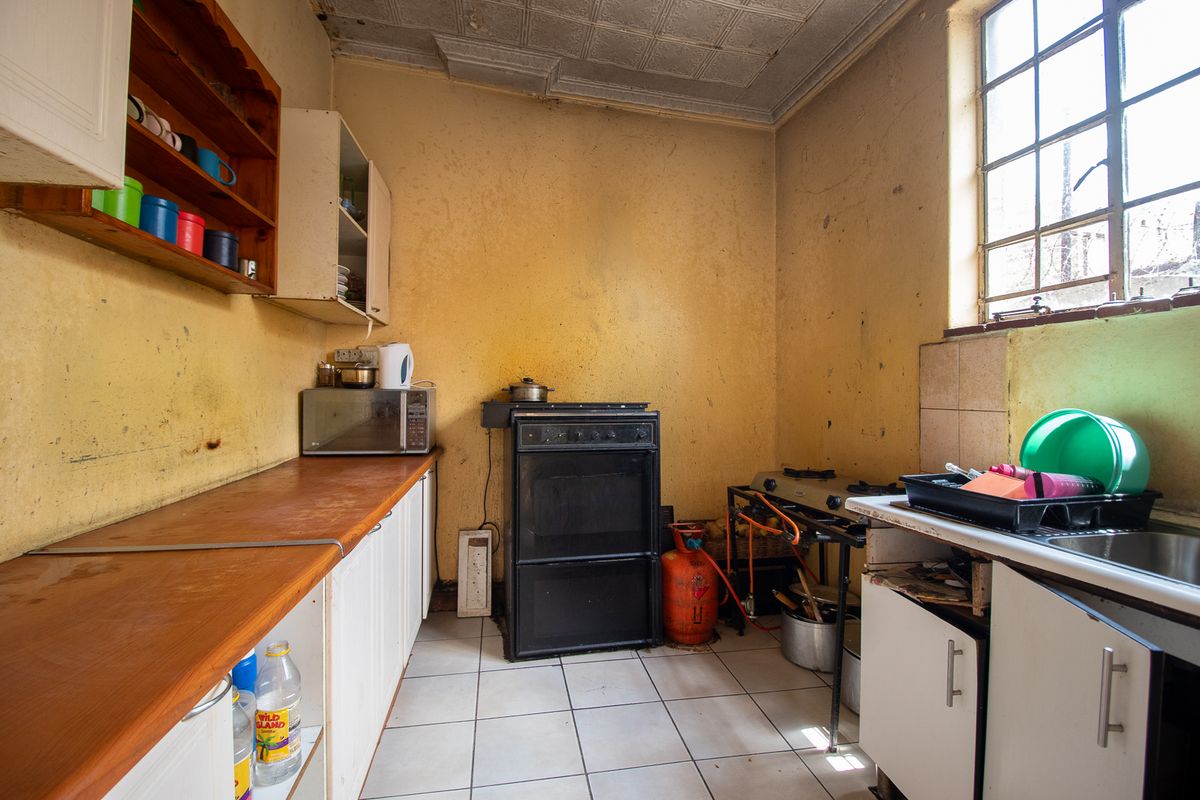 A dated kitchen featuring basic cabinetry, a freestanding oven, and a stainless steel sink, requiring significant renovation and cosmetic updates.