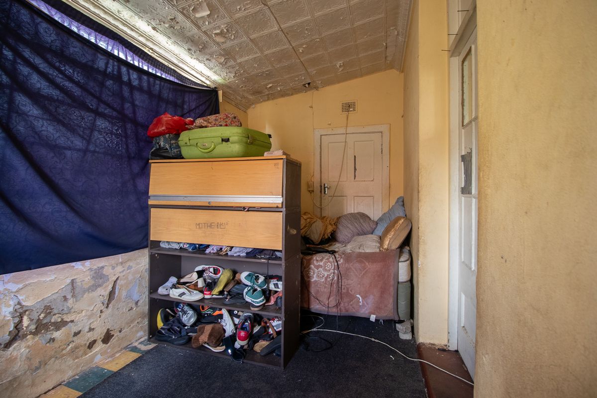 A bedroom featuring a traditional pressed metal ceiling and timber door, currently requiring significant restoration of wall and ceiling finishes.