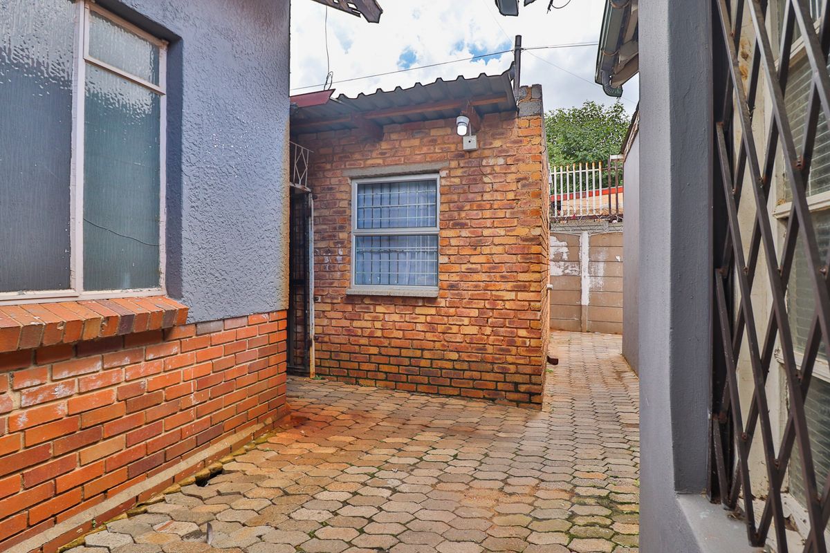 A narrow rear exterior courtyard featuring brick paving, exposed brick walls, and security-fitted windows between two sections of the property.