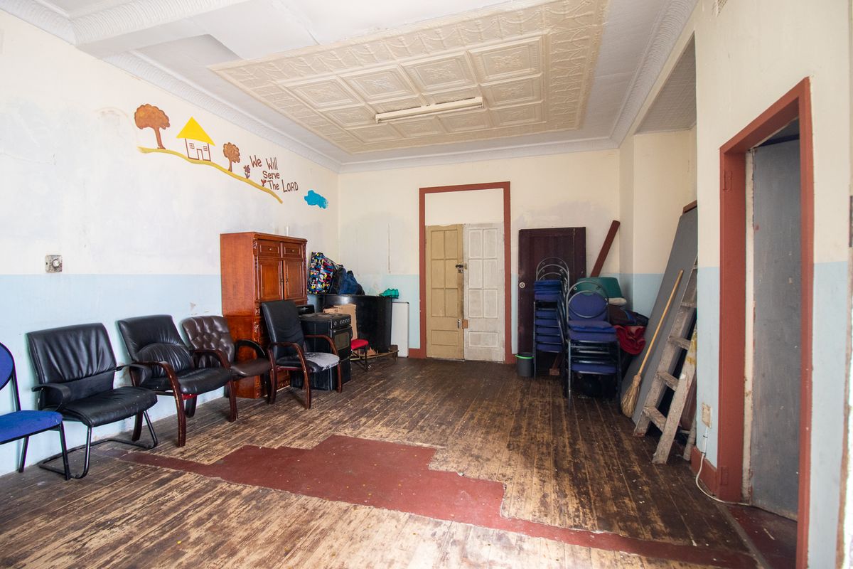 Spacious living area featuring original pressed metal ceilings and timber flooring, requiring significant cosmetic renovation and restoration to restore its character.