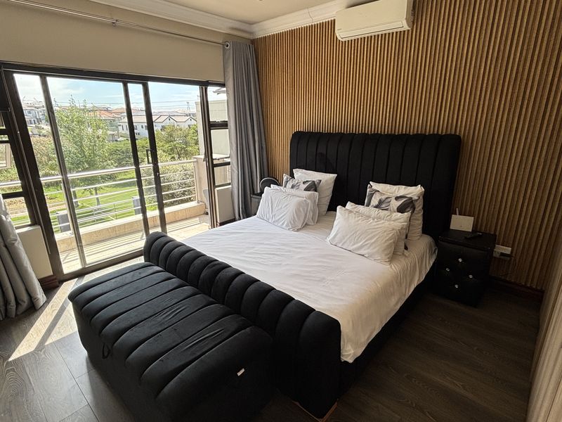 A well-maintained bedroom featuring a timber slat accent wall, split-system air conditioning, built-in wardrobes, and direct access to a private balcony.