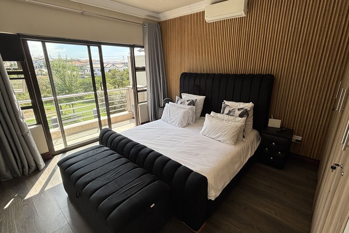 A well-maintained bedroom featuring a timber slat accent wall, split-system air conditioning, built-in wardrobes, and direct access to a private balcony.