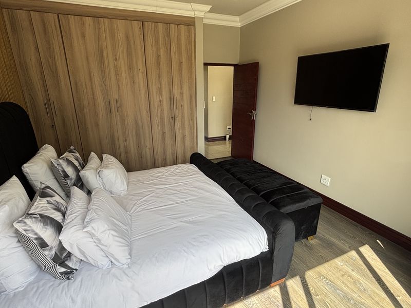 A well-maintained bedroom featuring modern laminate flooring, neutral wall tones, and extensive built-in wooden cupboards for ample storage.