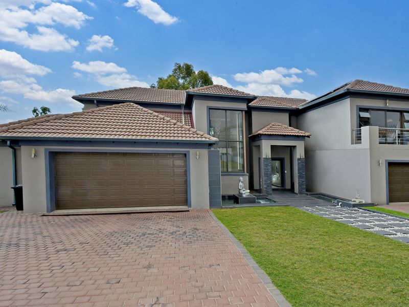 Modern double-story residence featuring a multi-car garage, paved driveway, stone-accented facade, and a balcony overlooking the landscaped front garden.