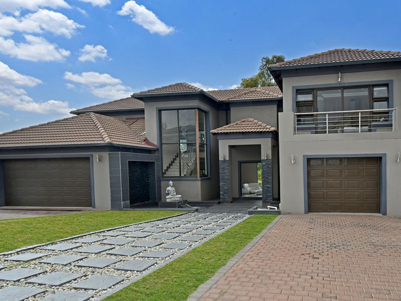 Modern double-story residence featuring a multi-car garage, stone-accented facade, paved driveway, and a balcony overlooking the front garden.