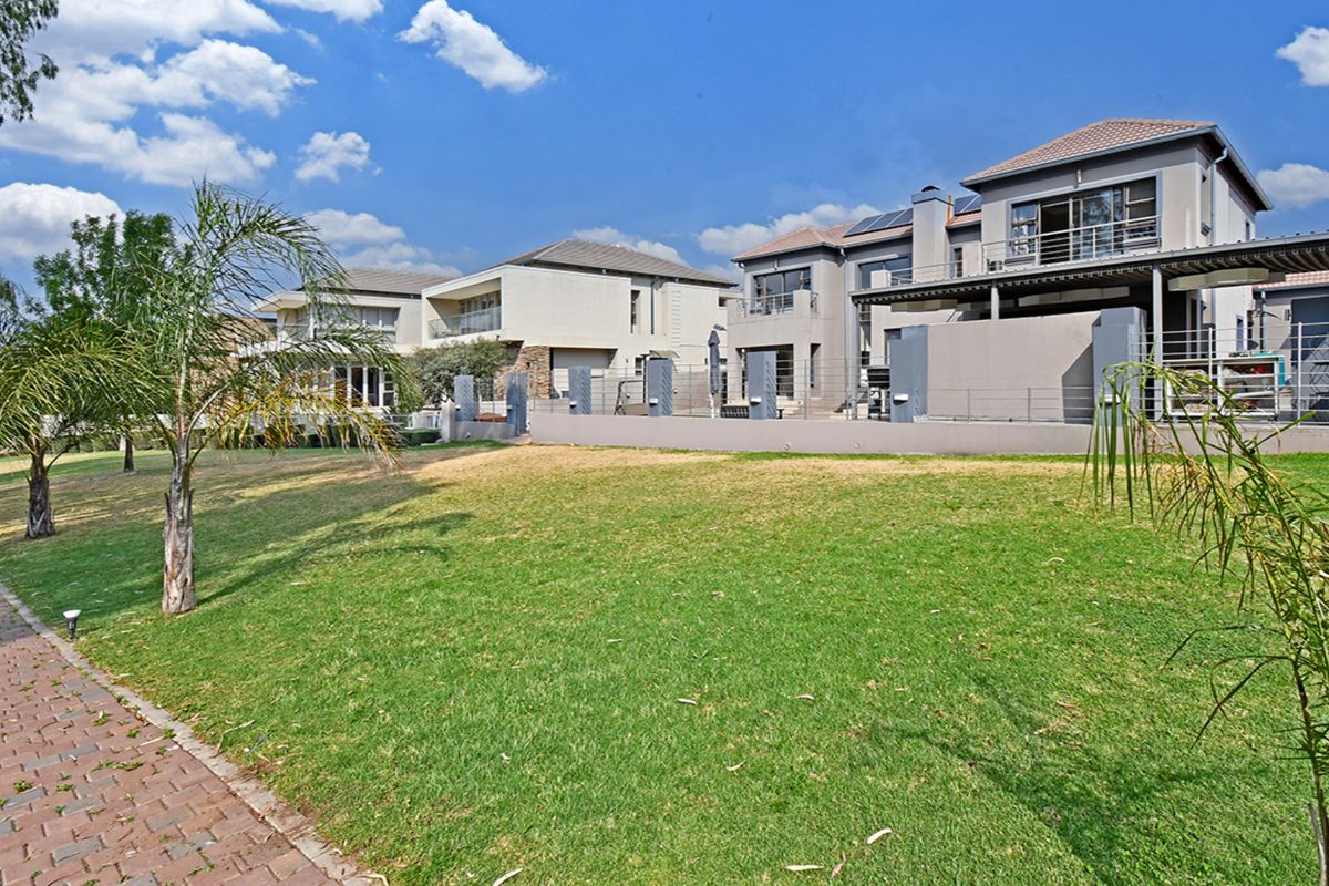 A view of the rear exterior of a modern multi-story house featuring a landscaped lawn, paved walkway, and elevated balconies.