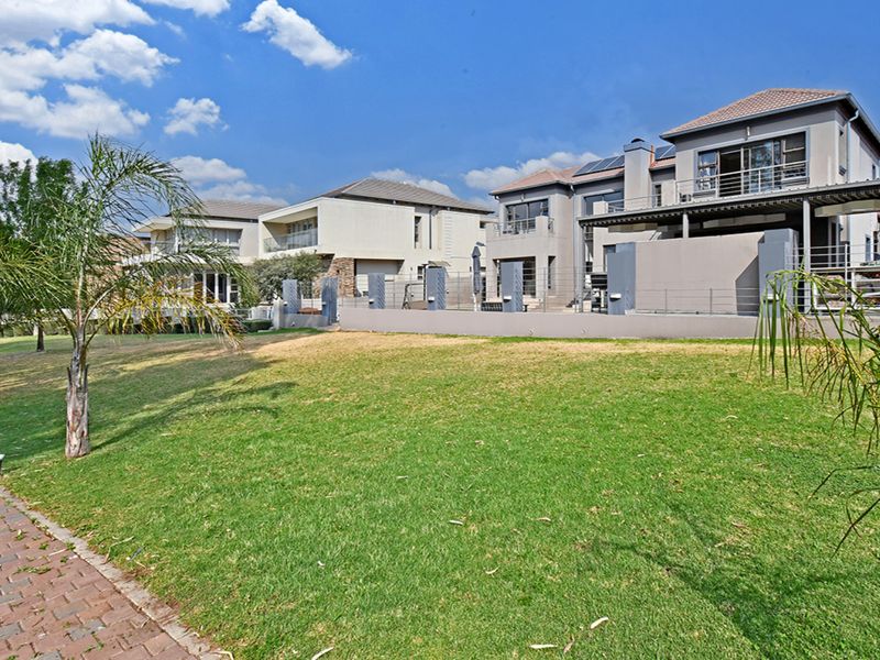 A view of the rear exterior of a modern multi-story house featuring a landscaped lawn, paved walkway, and elevated balconies.