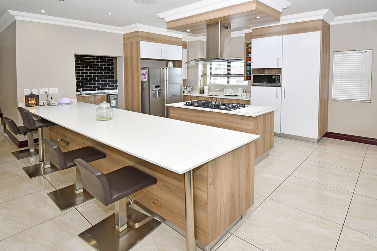 Modern kitchen featuring a large island with stone countertops, gas hob, integrated appliances, and sleek cabinetry with recessed lighting.