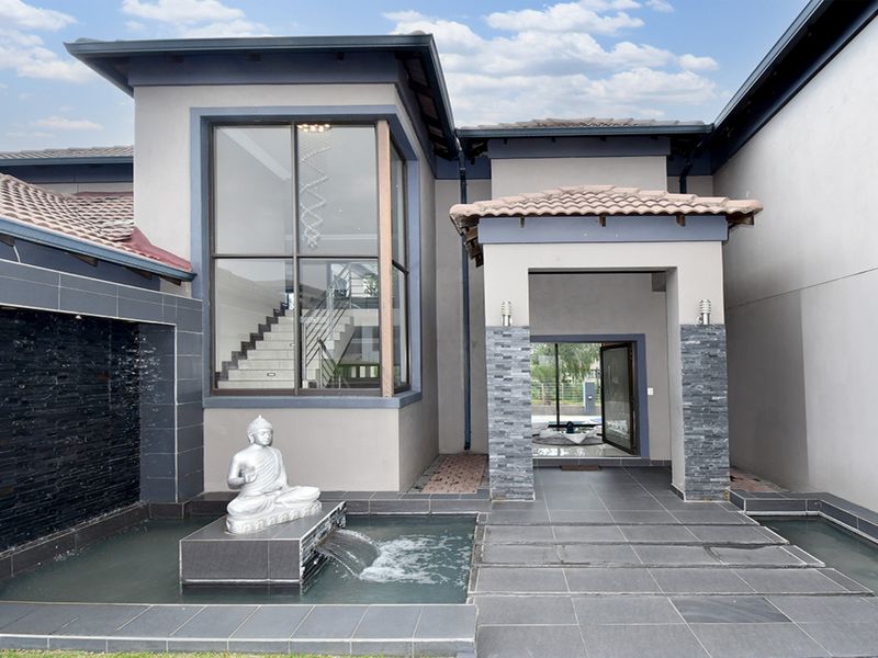 Modern front entrance featuring a decorative water feature, stone-clad pillars, and a large glass window showcasing the interior staircase.