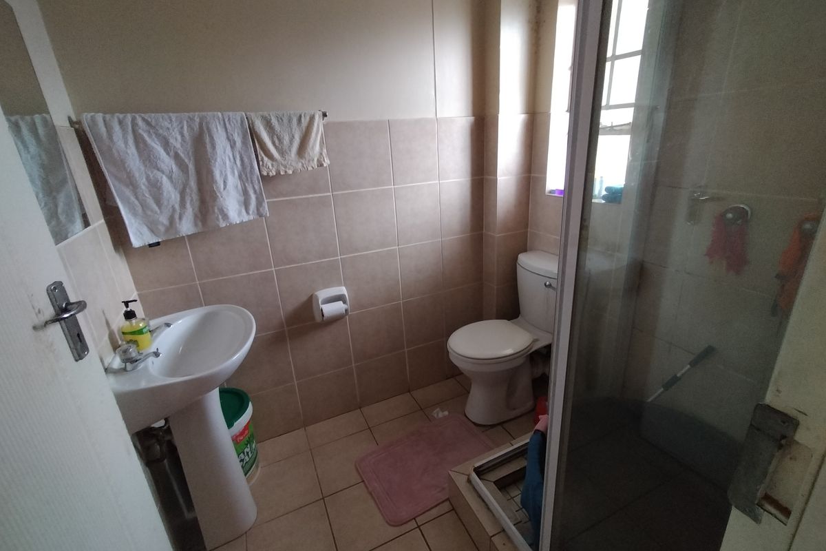 A functional bathroom featuring a pedestal basin, toilet, and a shower enclosure with tiled finishes, requiring some maintenance and cosmetic updates.