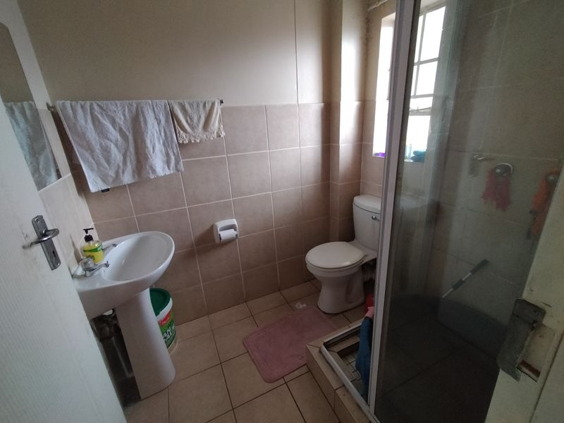 A functional bathroom featuring a pedestal basin, toilet, and a shower enclosure with tiled finishes, requiring some maintenance and cosmetic updates.
