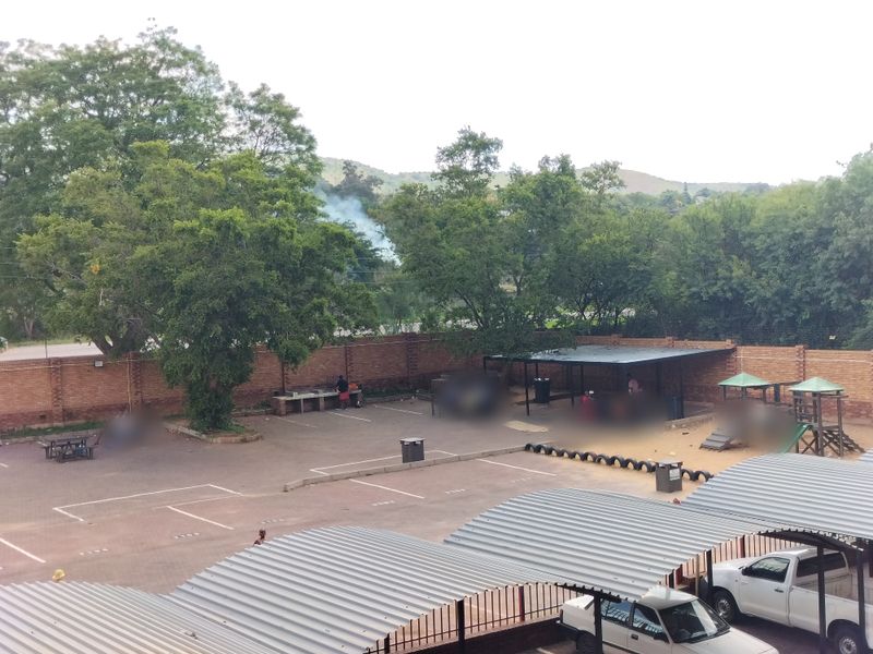 Communal outdoor area featuring paved parking bays, covered parking structures, a brick boundary wall, and a children's play area.