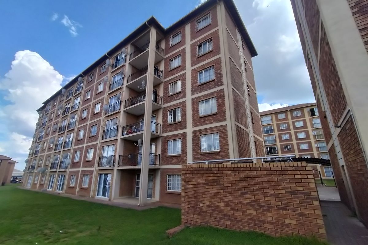 Exterior view of a multi-story apartment complex featuring face brick construction, private balconies with metal railings, and surrounding communal lawn areas.