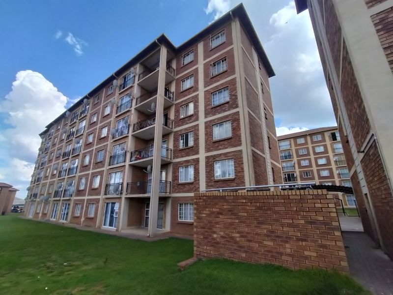 Exterior view of a multi-story apartment complex featuring face brick construction, private balconies with metal railings, and surrounding communal lawn areas.