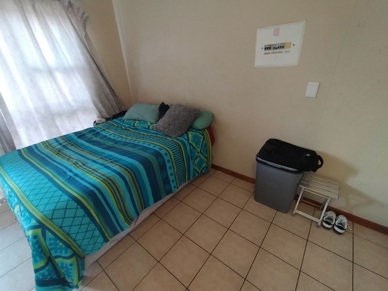 A functional bedroom featuring tiled flooring and a wall-mounted electrical distribution board, providing a simple and practical living space.