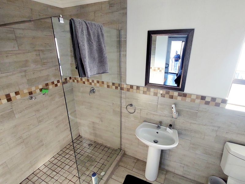 A functional bathroom featuring a glass-enclosed shower, pedestal sink, toilet, and neutral-toned wall and floor tiling.