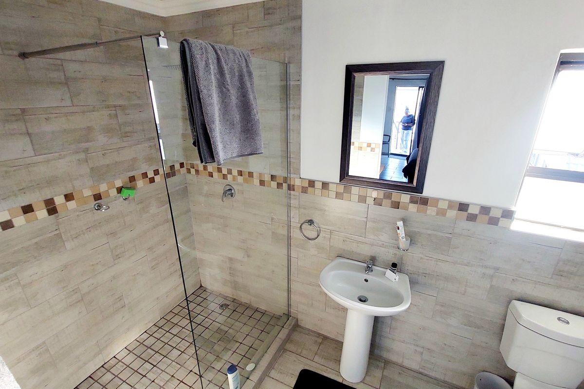 A functional bathroom featuring a glass-enclosed shower, pedestal sink, toilet, and neutral-toned wall and floor tiling.