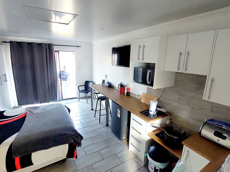 Open-plan studio apartment featuring a compact kitchenette with built-in cabinetry, tiled flooring, and direct access to an outdoor area via a sliding glass door.