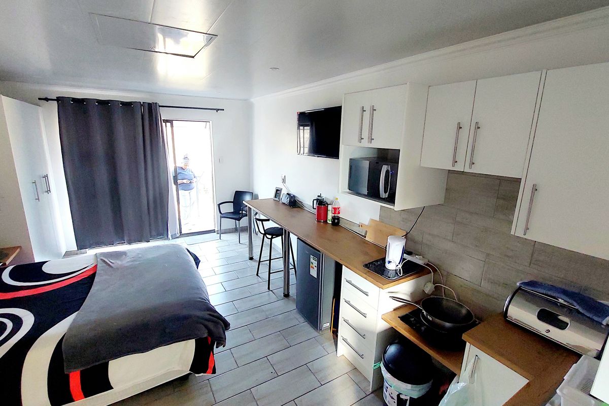 Open-plan studio apartment featuring a compact kitchenette with built-in cabinetry, tiled flooring, and direct access to an outdoor area via a sliding glass door.