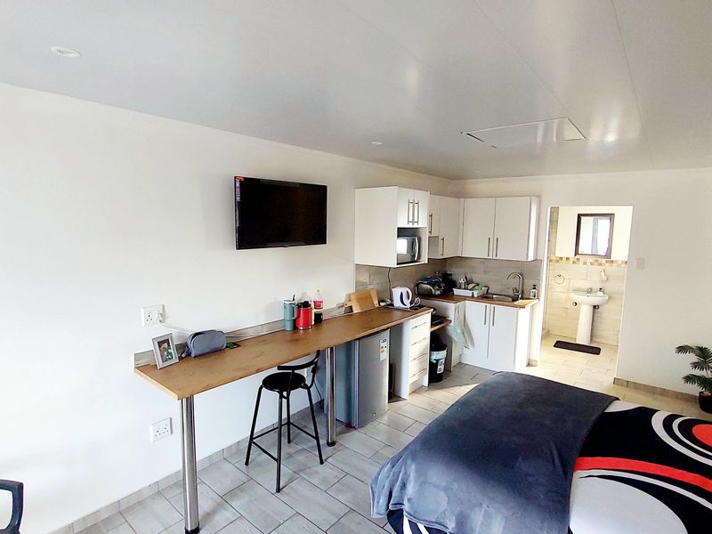 Open-plan studio apartment featuring a compact kitchenette with built-in cabinetry, tiled flooring, and an adjoining bathroom with a pedestal basin.