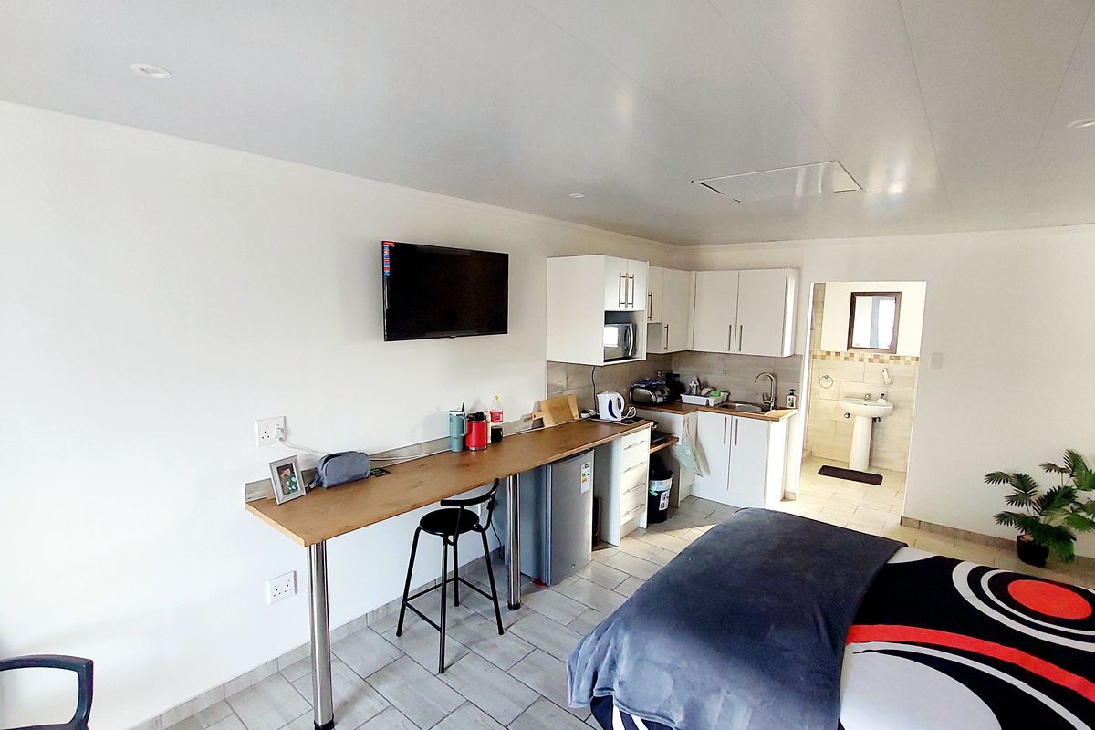 Open-plan studio apartment featuring a compact kitchenette with built-in cabinetry, tiled flooring, and an adjoining bathroom with a pedestal basin.