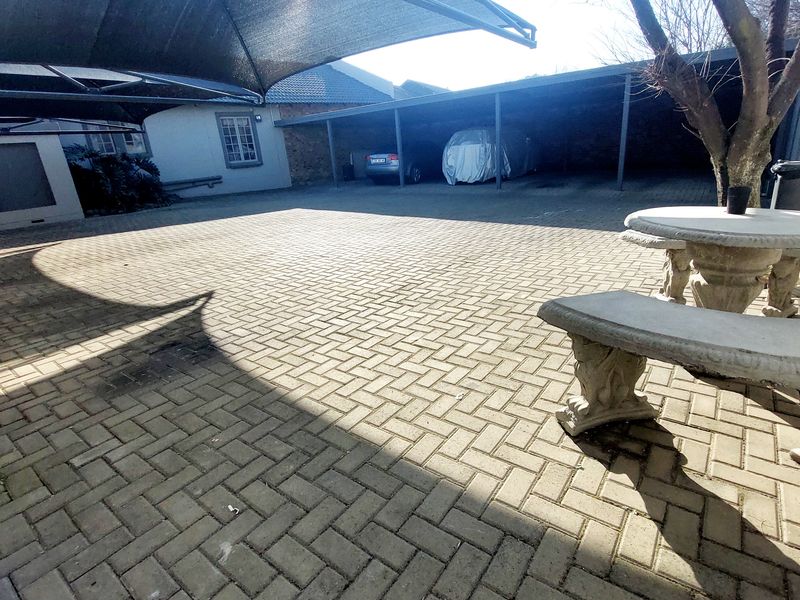 A paved outdoor parking area featuring a covered carport structure and shade sail, providing functional vehicle storage space.