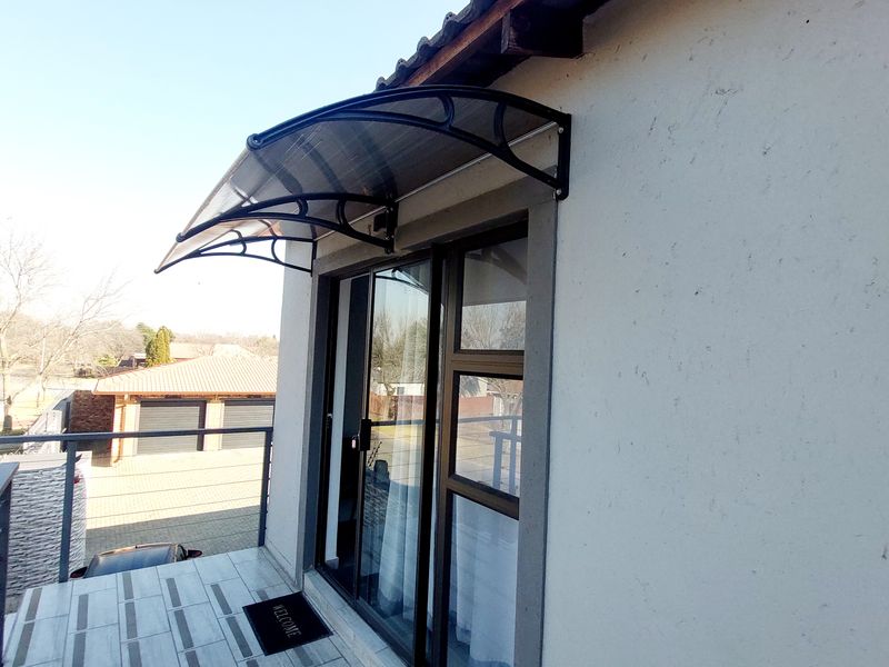 A clean balcony area featuring a modern sliding glass door, a protective polycarbonate awning, and tiled flooring with metal safety railings.