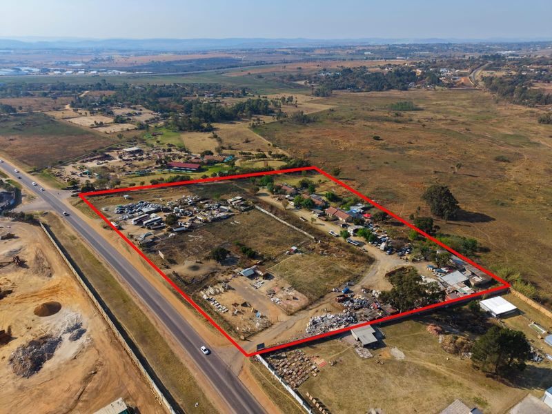Aerial view of a large plot of land featuring multiple outbuildings, perimeter fencing, and direct access to a main road.