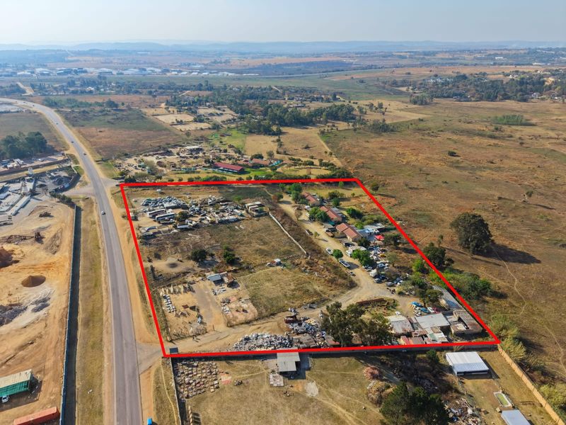 Aerial view of a large plot of land featuring multiple outbuildings, perimeter fencing, and significant open space with road access.