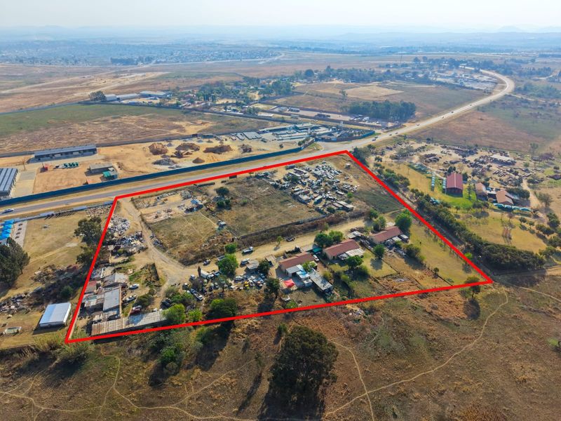 Aerial view of a large property plot with multiple outbuildings, extensive open land, and perimeter fencing, situated near a main road.