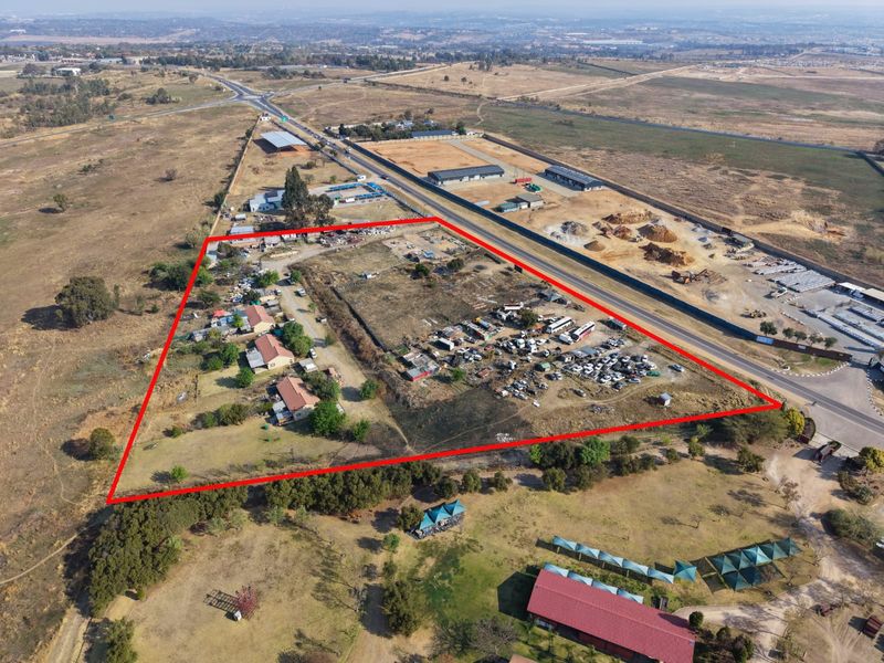 Aerial view of a large, undeveloped plot of land with existing structures, outlined in red, situated near a main road.
