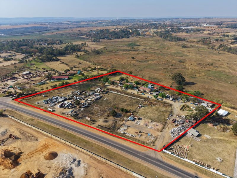 Aerial view of a large plot of land with existing structures and perimeter fencing, situated adjacent to a main road.