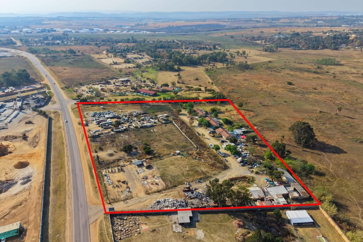 Aerial view of a large plot of land featuring multiple outbuildings, perimeter fencing, and significant open space with road access.