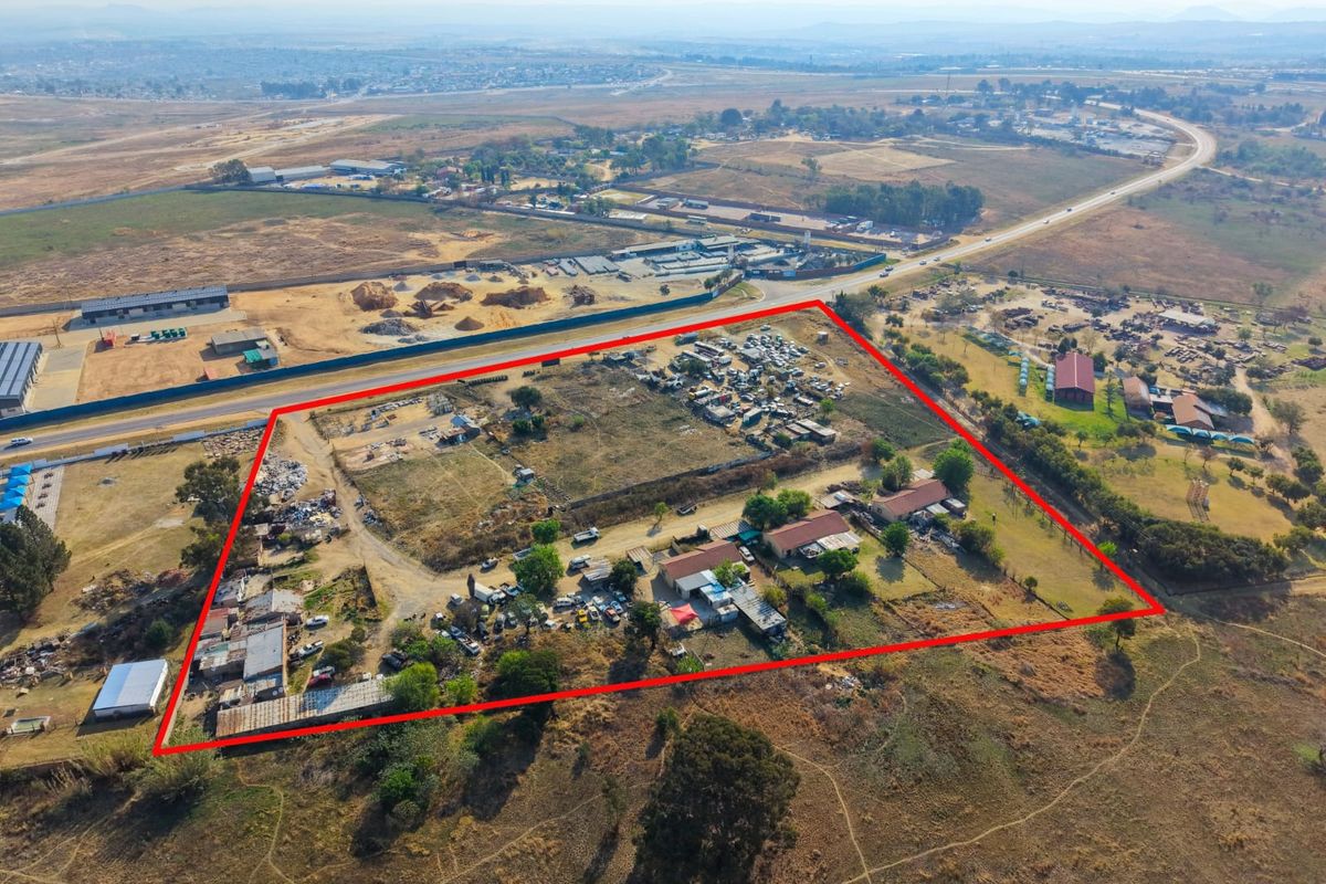 Aerial view of a large property plot with multiple outbuildings, extensive open land, and perimeter fencing, situated near a main road.