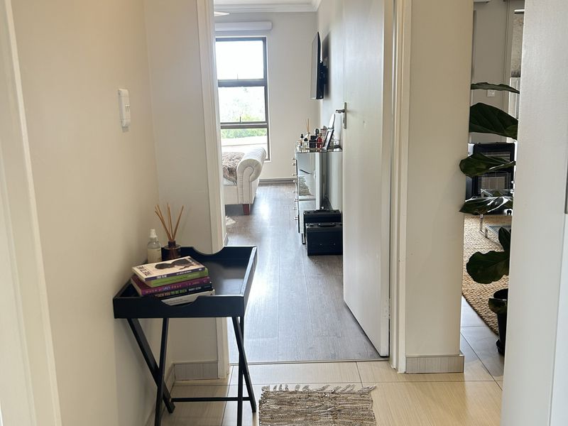 A bright, neutral-toned hallway featuring tiled flooring that transitions into laminate flooring, connecting the main living areas with recessed downlighting throughout.