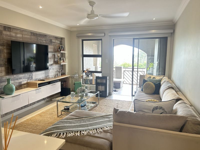 A well-maintained living room featuring a wood-look accent wall, built-in media cabinetry, recessed lighting, and direct access to a private balcony.