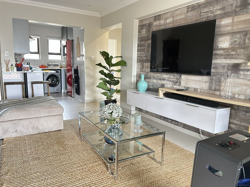 Open-plan living area featuring a modern media wall with wood-look cladding, tiled floors, and a seamless transition into the adjacent kitchen space.