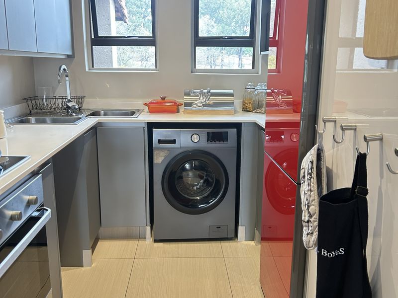 A modern, compact kitchen featuring grey cabinetry, tiled flooring, built-in oven, and integrated laundry appliances under a clean countertop.