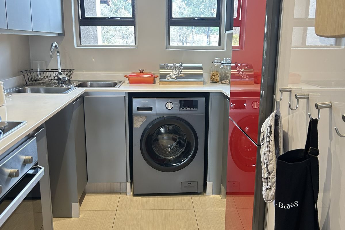 A modern, compact kitchen featuring grey cabinetry, tiled flooring, built-in oven, and integrated laundry appliances under a clean countertop.