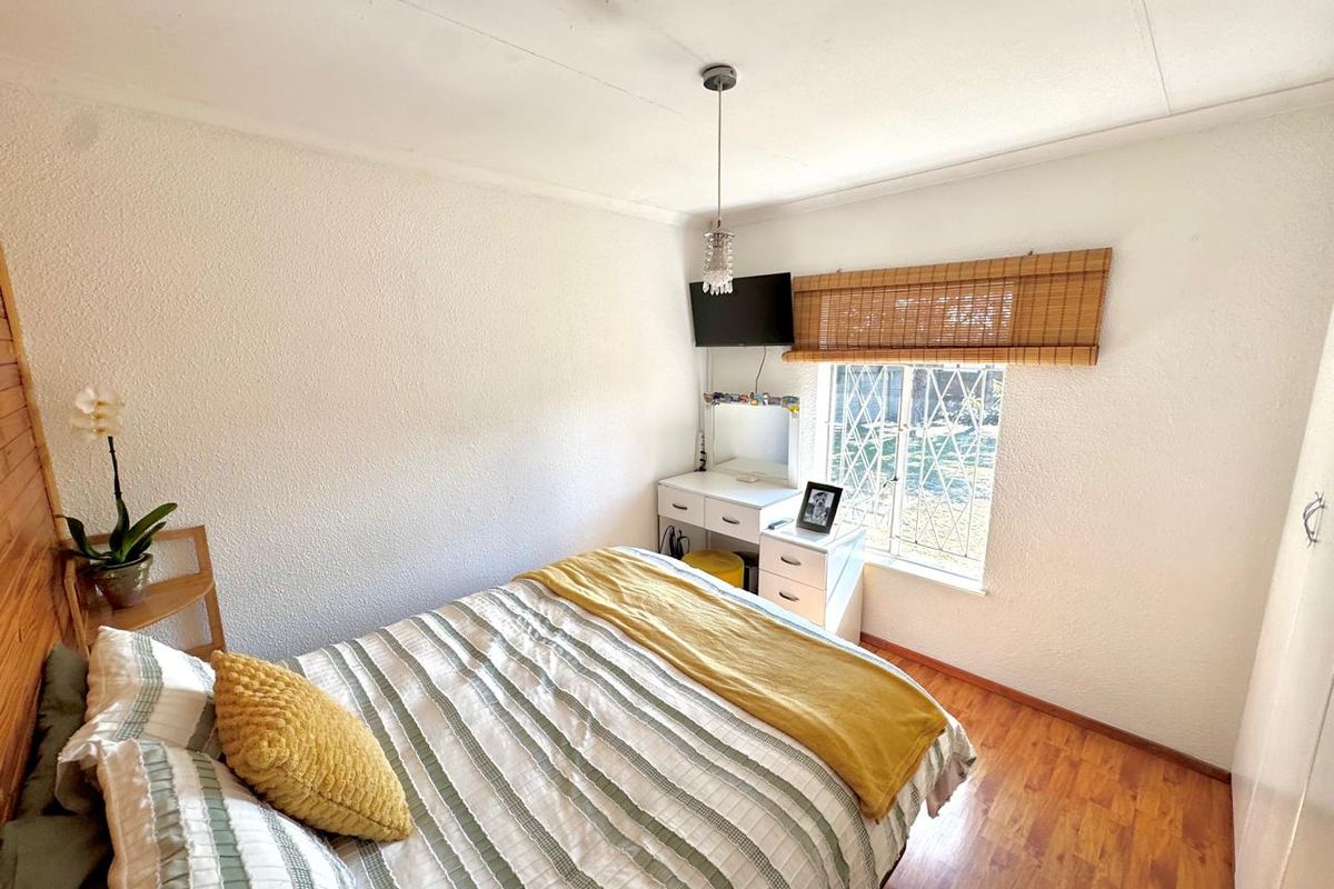 A cozy bedroom featuring laminate flooring, a window with security bars, and a built-in wardrobe, offering a functional and well-lit living space.