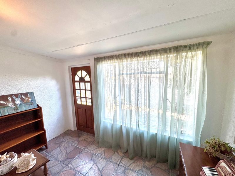 A living area featuring stone-look floor tiles, a timber-framed entrance door, and large windows fitted with security bars.