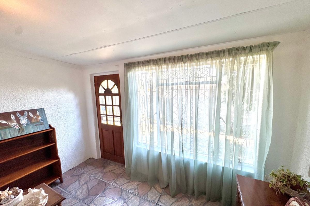 A living area featuring stone-look floor tiles, a timber-framed entrance door, and large windows fitted with security bars.
