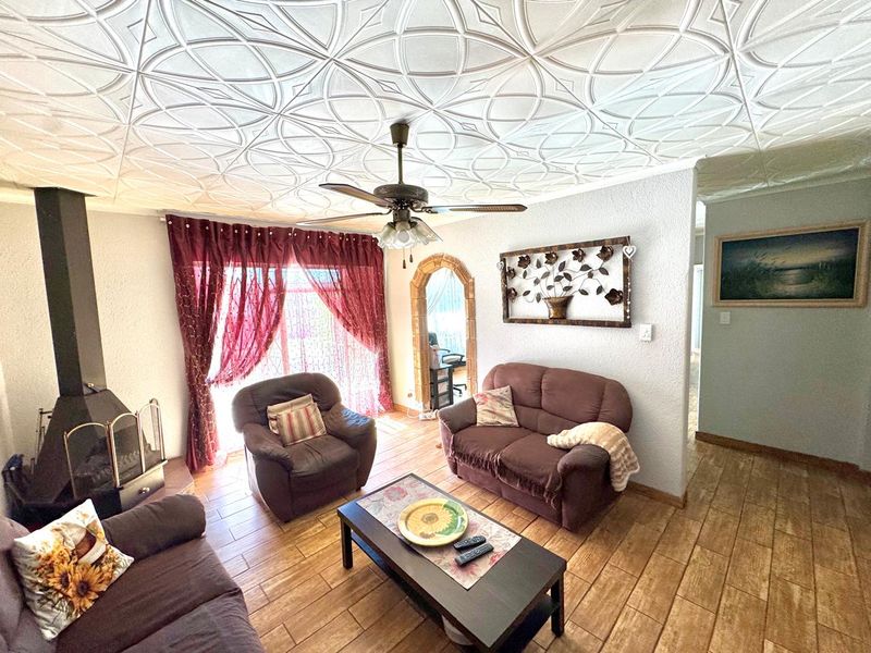 Living room featuring a wood-burning fireplace, decorative ceiling tiles, ceiling fan, and tiled flooring with an arched transition to adjacent spaces.